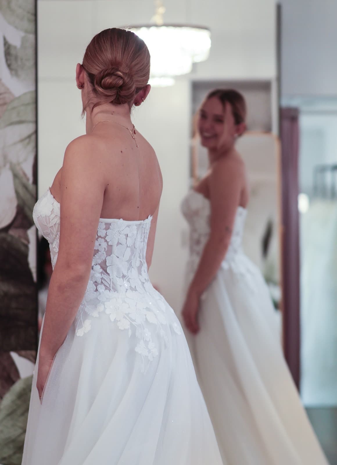 Braut von hinten vor dem Spiegel im Off-Shoulder-Kleid — Anprobe-Moment bei Liebesgeschichte