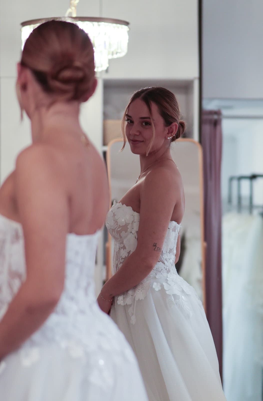 Strahlende Braut betrachtet sich lächelnd im Spiegel — Off-Shoulder-Brautkleid mit Blumenapplikation