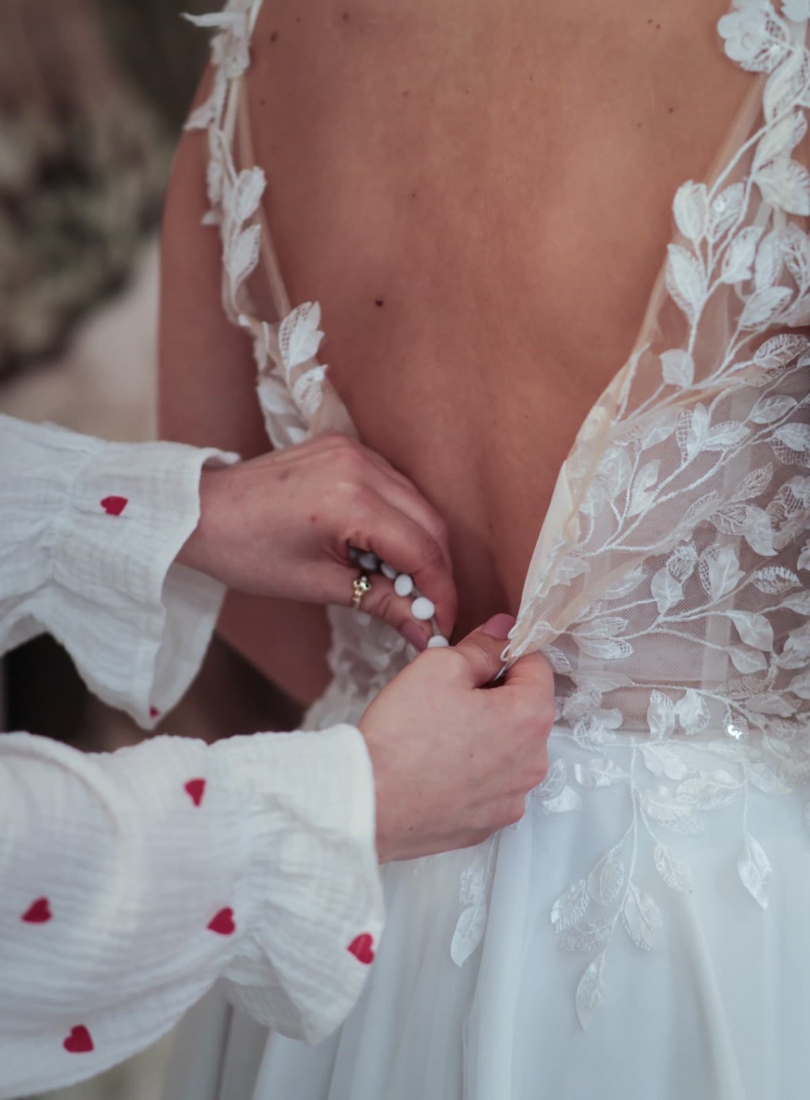 Liebevolles Zuknöpfen eines Brautkleids mit Blätterapplikation — Brautmode-Beratung Königsbach-Stein